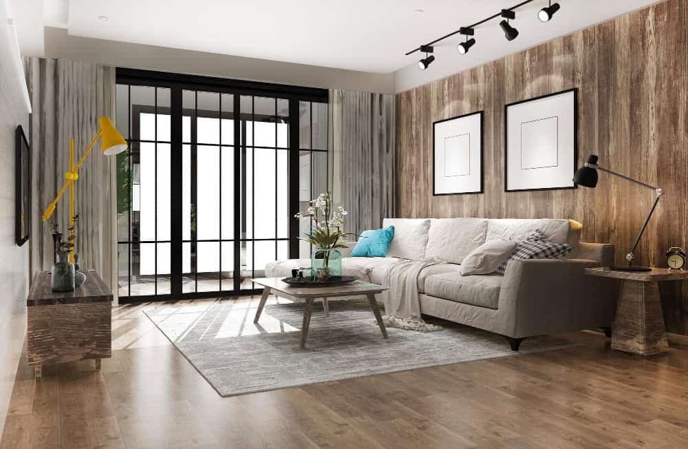 Salón moderno con suelo de madera, sofá claro y ventanales amplios, representando el estilo de viviendas disponibles para compra en Madrid con asesoramiento profesional.